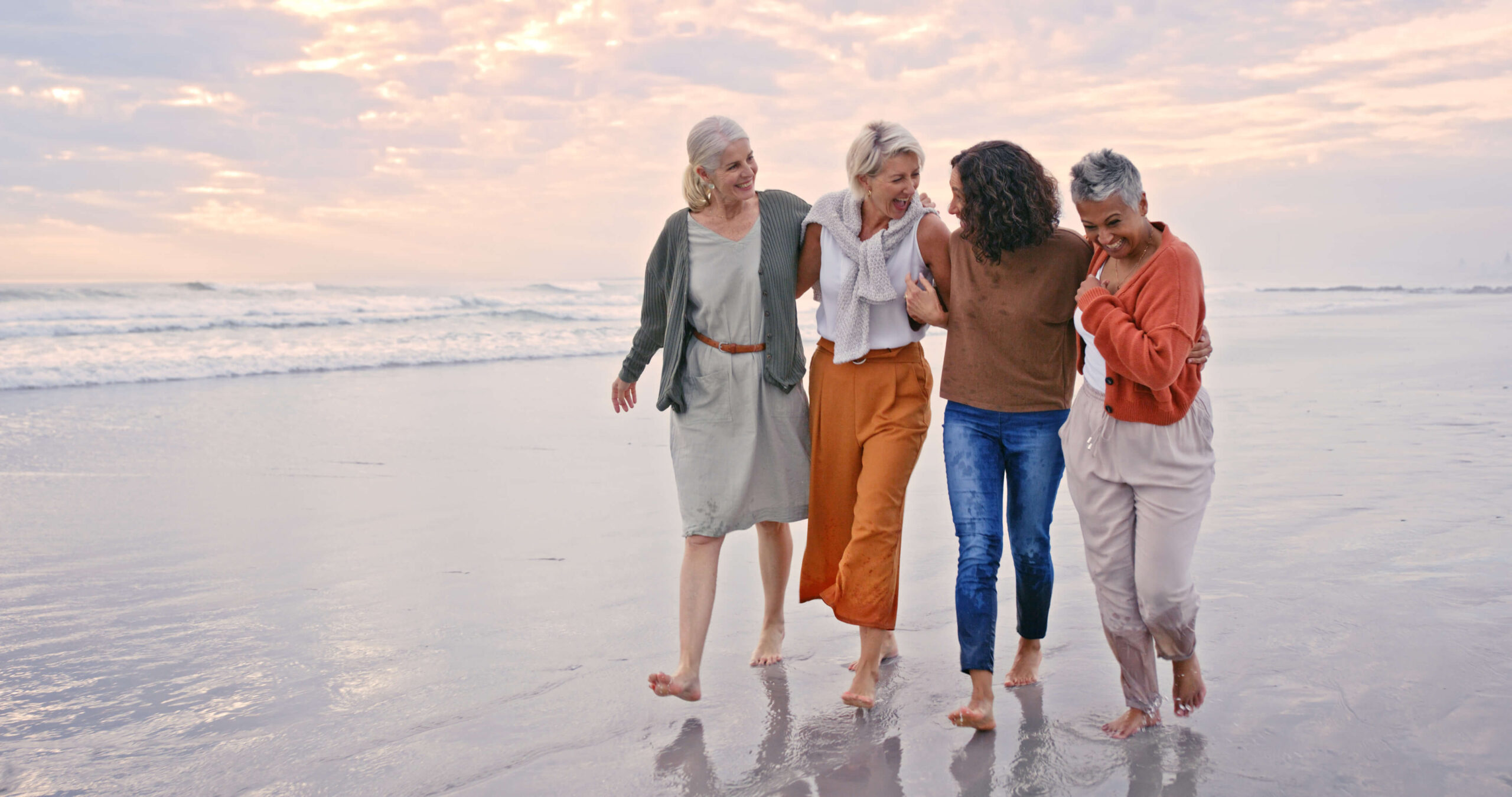 Happy, women and friends on beach, walking and connect on vacation, holiday and bonding together outdoor. Diversity, retirement and senior females talking, stroll and seaside vacation and sunset.